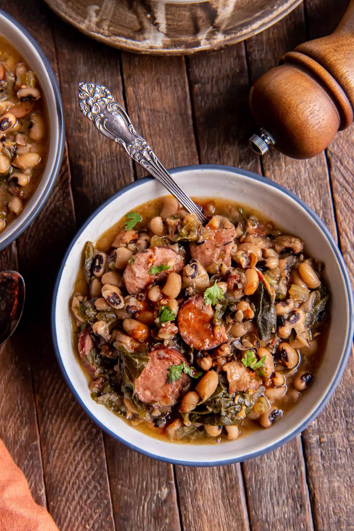 A spoon resting in a bowl of black eyed peas on a dark wood board.