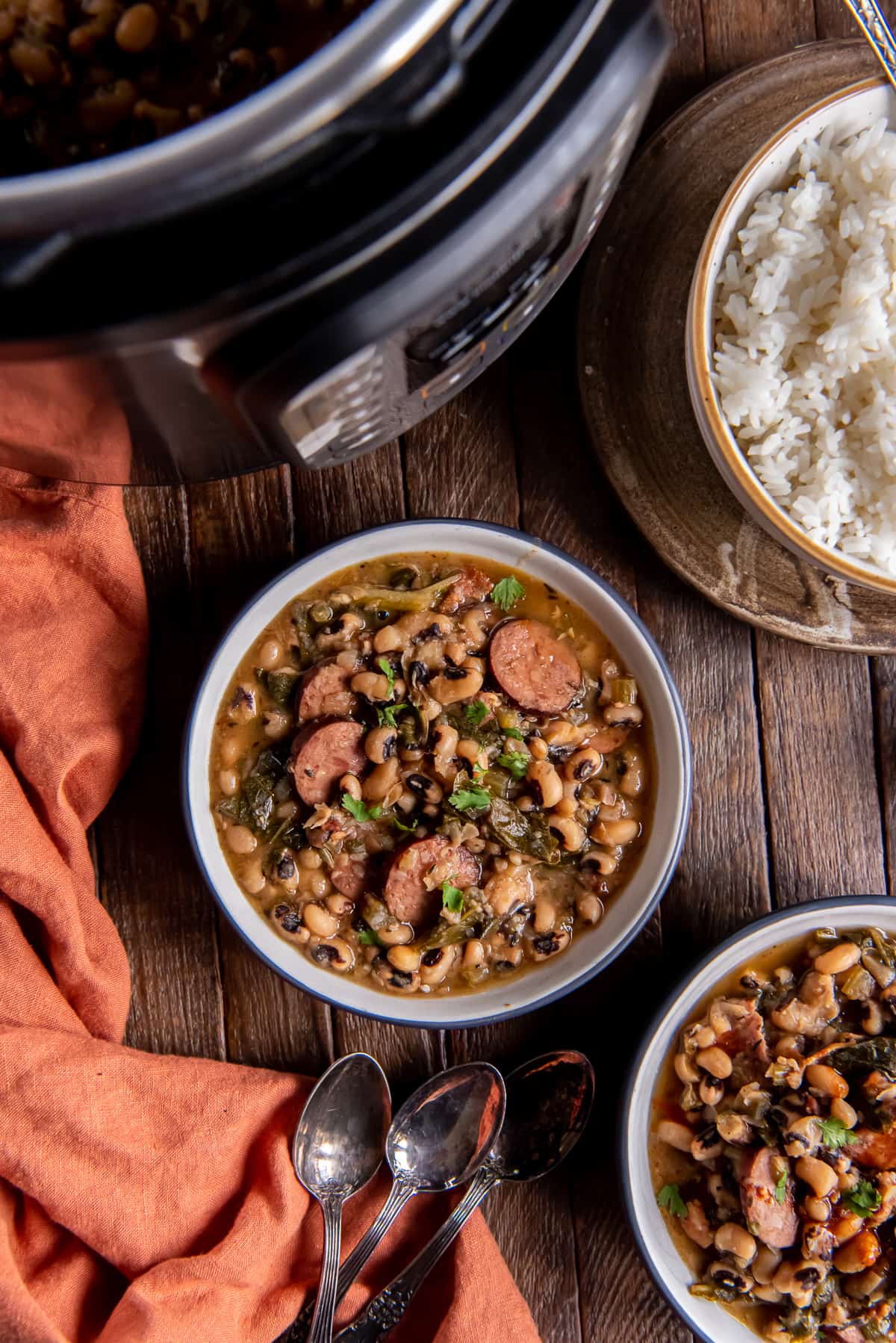 A top down shot of two bowls of black cowpeas with sausage on a dark wooden board.