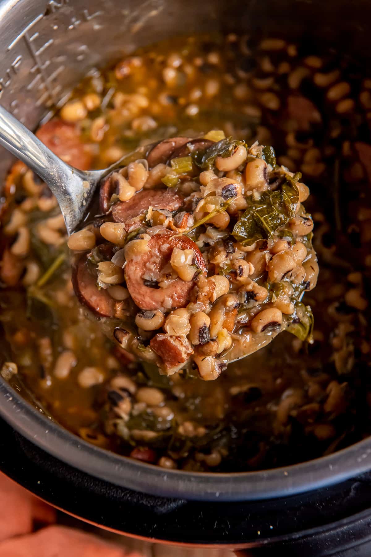 A ladle scooping Black Eyed Peas with collards and sausage from an Instant Pot.