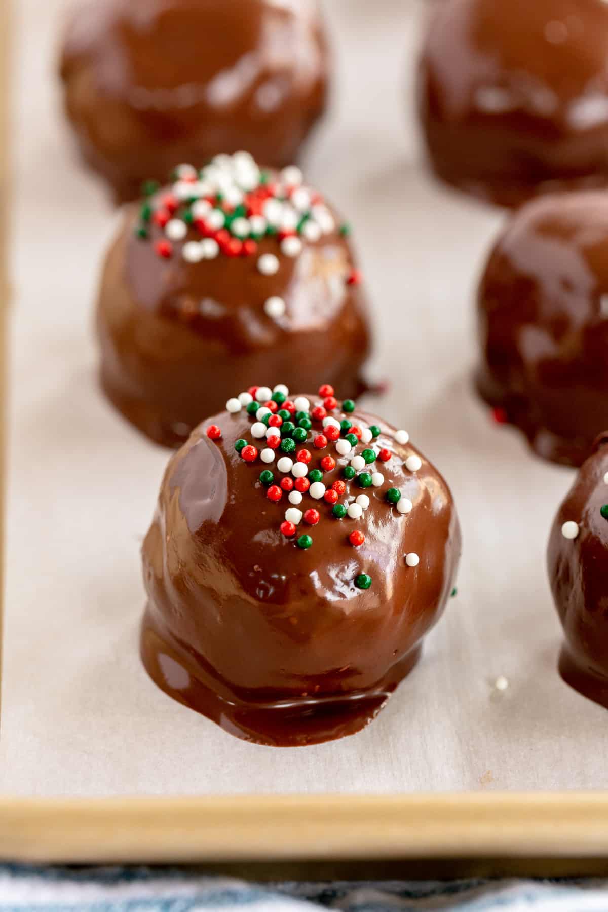 Chocolate bon bons with  red and green sprinkles drying on a parchment paper lined baking sheet.