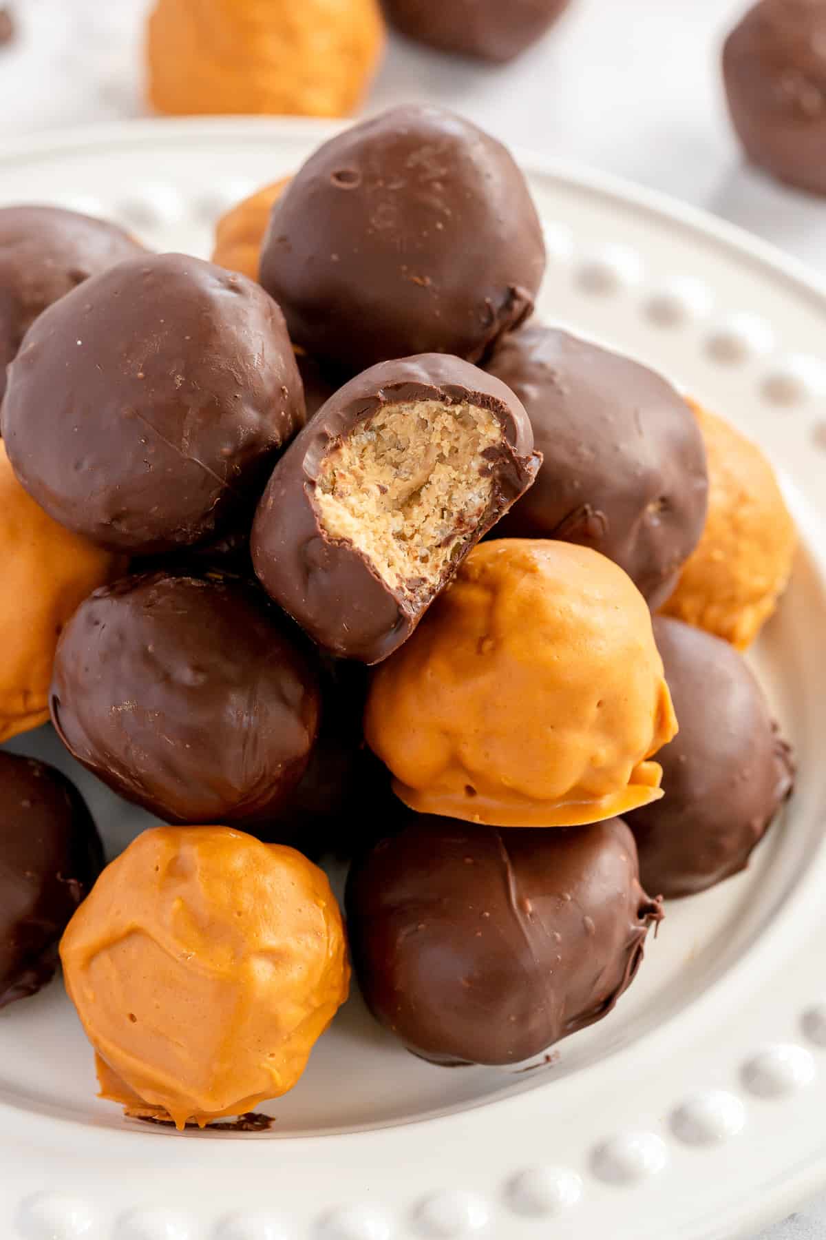 A chocolate coated bon bon with a bite missing on top of a stack on a white plate.