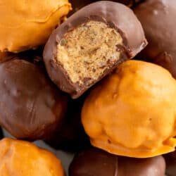 A close up of a chocolate coated bon bon with a bite missing on top of a stack.