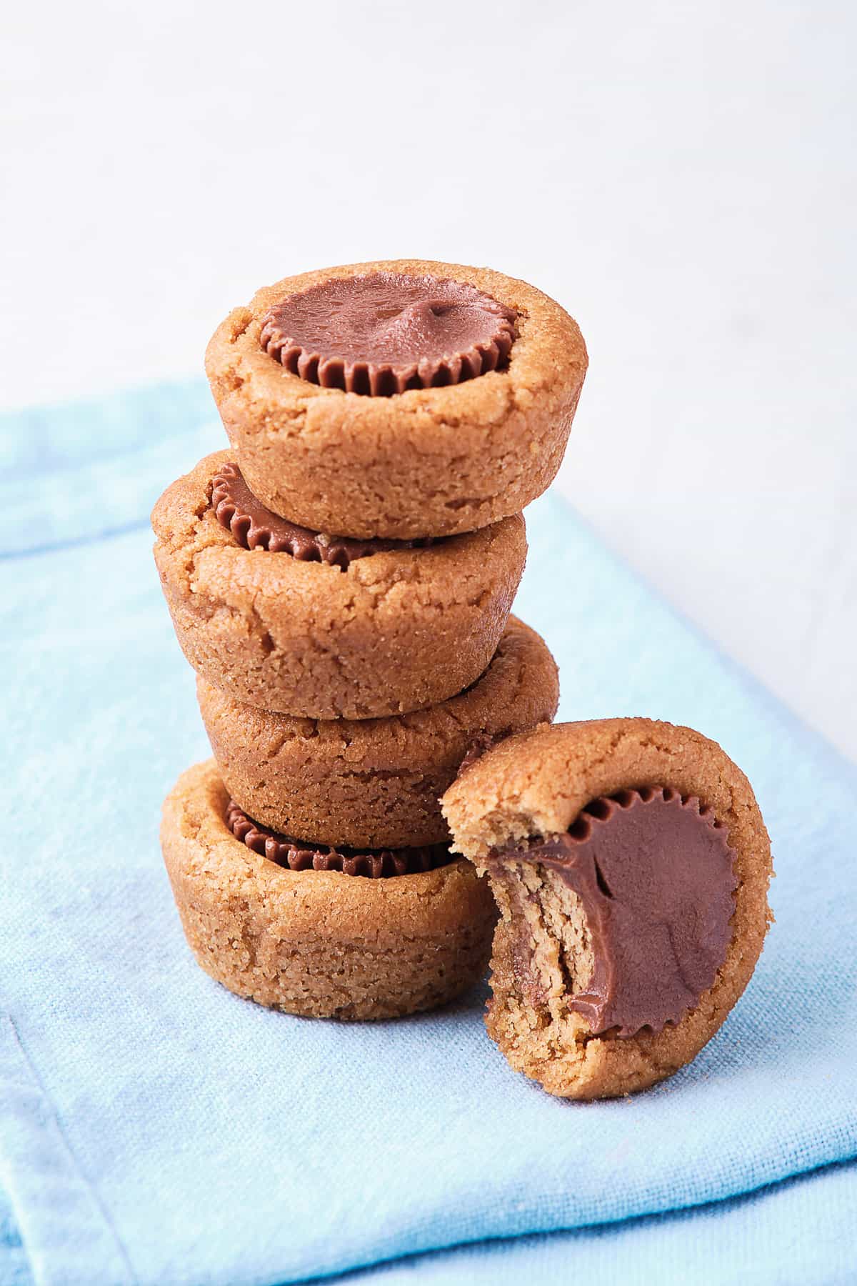A stack of four Peanut Butter Cookie Cups on a blue cloth with one with a bite missing leaning against it.