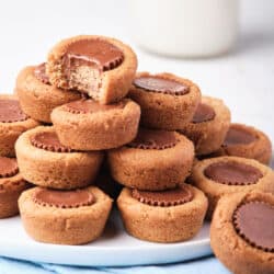Peanut Butter Cookie Cups piled on a white plate with a bite missing from the one on top.