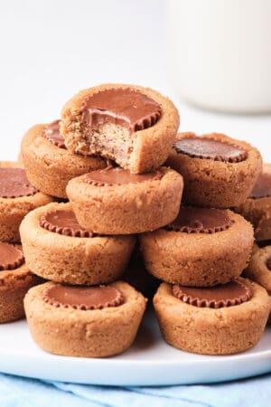 Peanut Butter Cookie Cups piled on a white plate with a bite missing from the one on top.