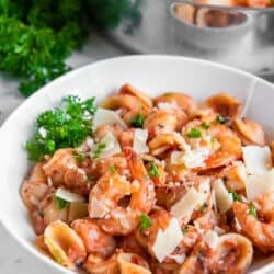 A white bowl filled with orecchiette pasta with shrimp in a vodka sauce garnished with fresh parsley.