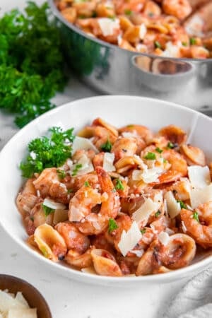 A white bowl filled with orecchiette pasta with shrimp in a vodka sauce garnished with fresh parsley.