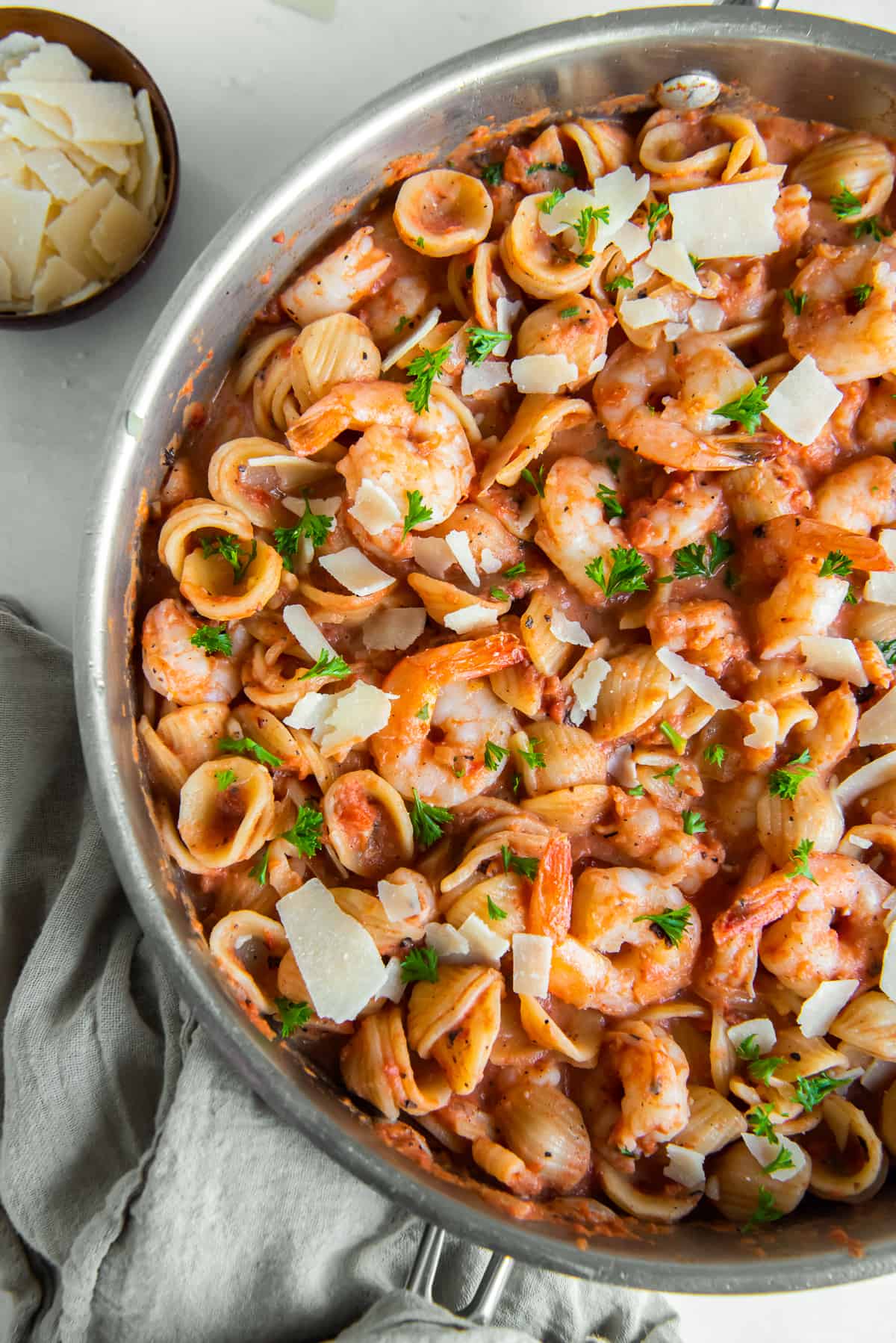 A top down shot of pasta with vodka sauce and shrimp topped with shaved Parmesan in a skillet.