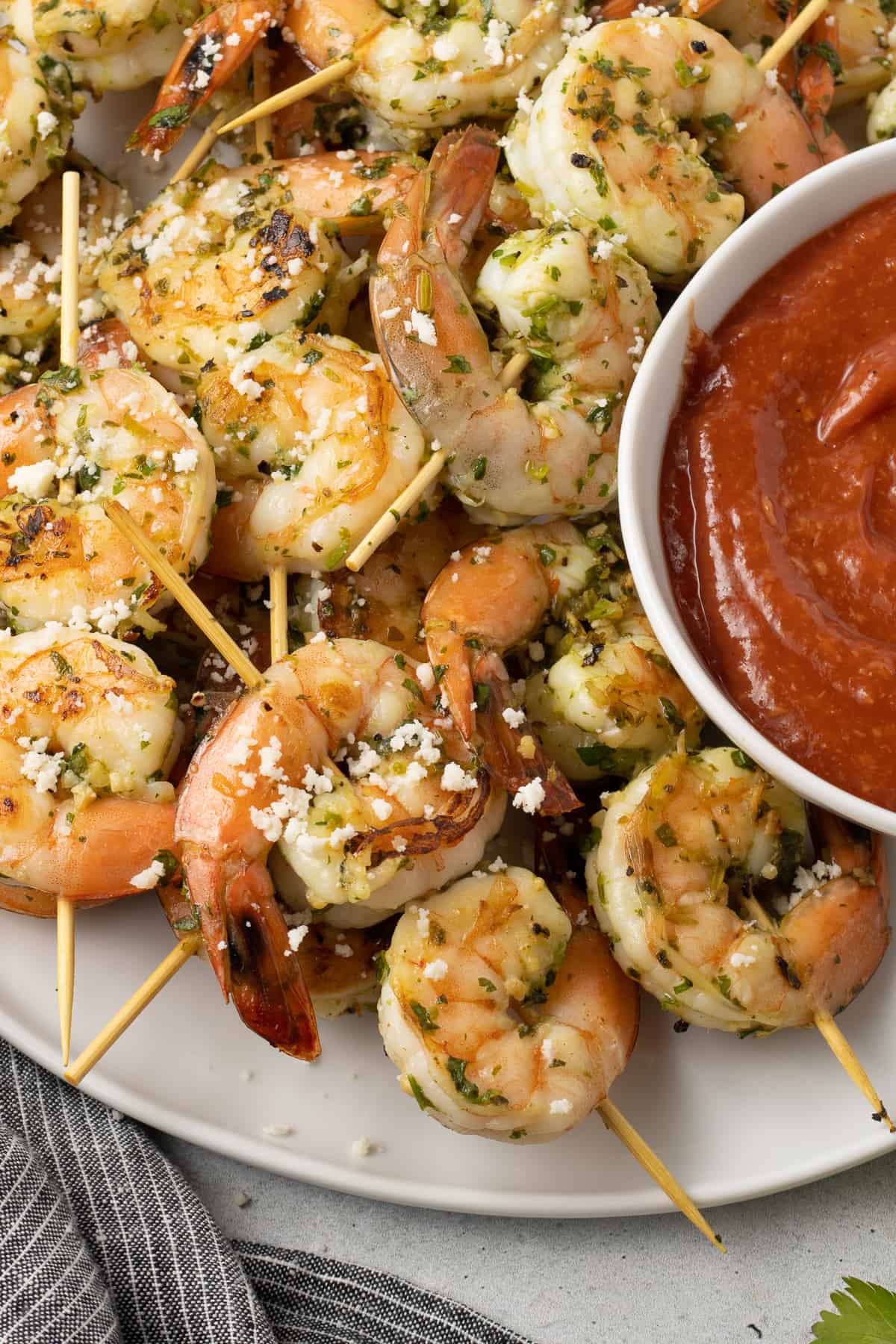 A close up of shrimp in skewers on a white platter with a small bowl of cocktail sauce.