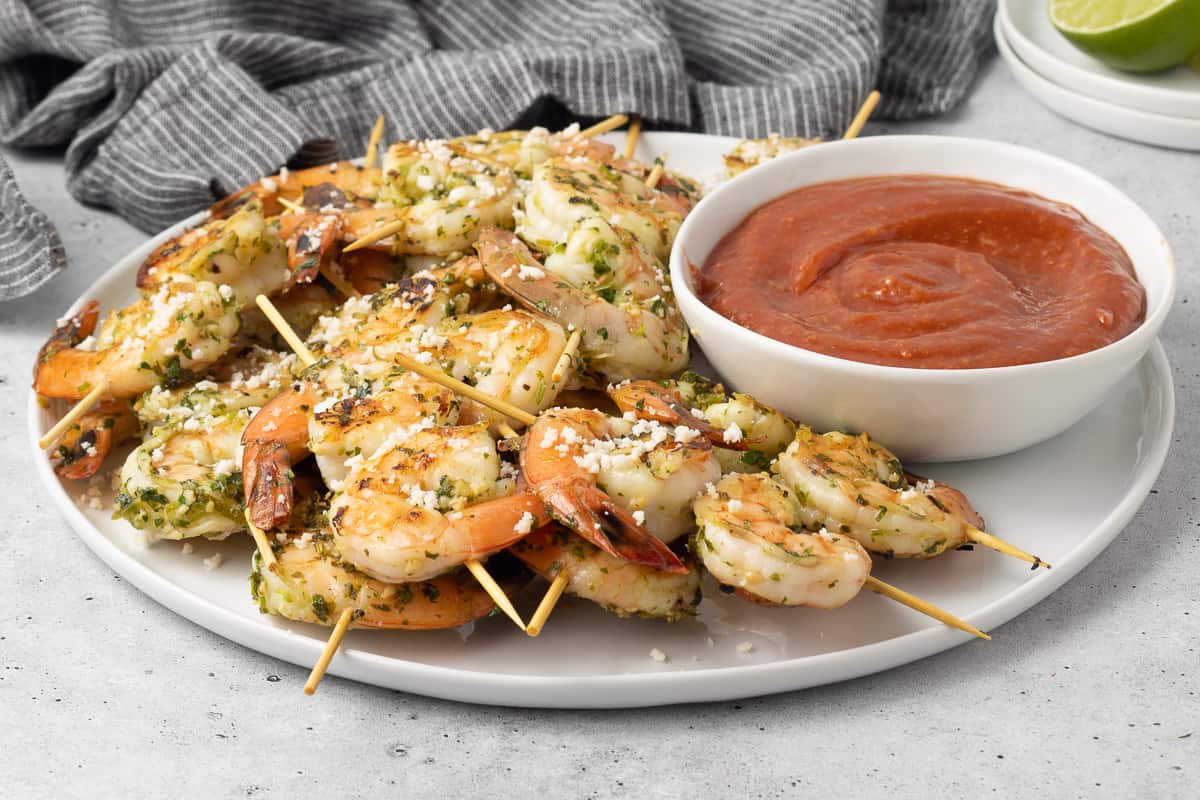 Shrimp skewers on a platter with a small bowl of cocktail sauce.