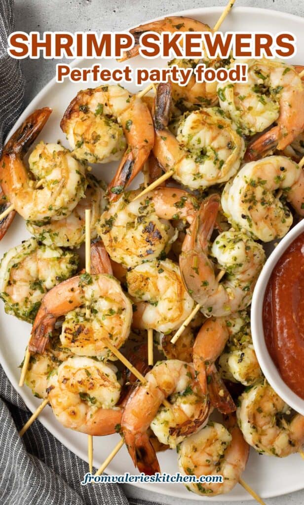 Shrimp skewers on a platter with cocktail sauce with text.