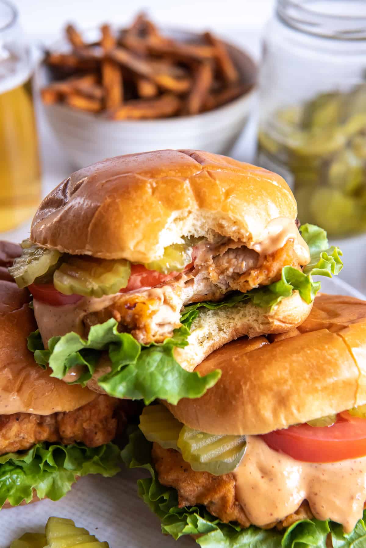 A crispy chicken sandwich on a brioche bun with a bite missing stacked on top of two others.