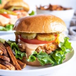 A crispy chicken sandwich with tomato pickles and lettuce on a plate with French Fries.