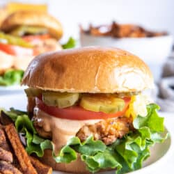 A crispy chicken sandwich with tomato pickles and lettuce on a plate with French Fries.