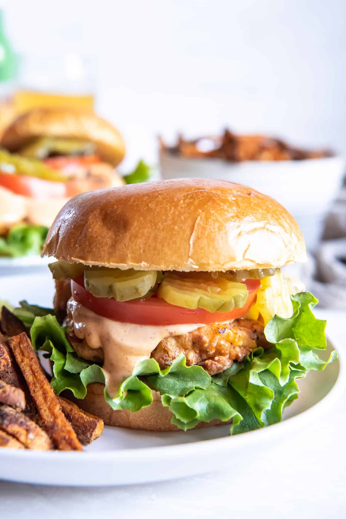 A crispy chicken sandwich with tomato pickles and lettuce on a plate with French Fries.