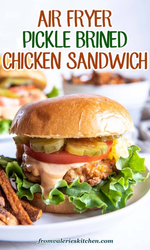A crispy chicken sandwich with tomato pickles and lettuce on a plate with French Fries with text.