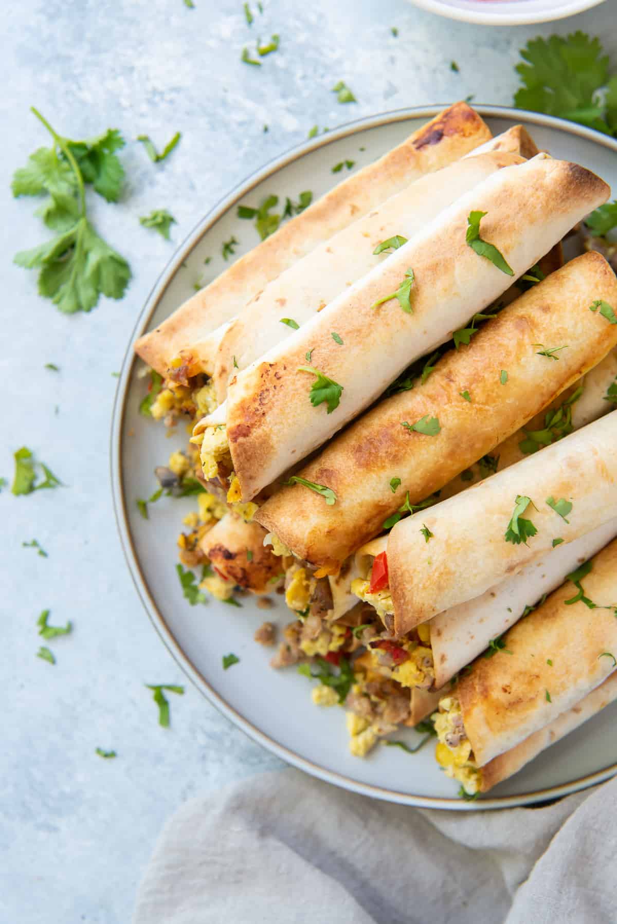 A top down shot of breakfast taquitos stacked on a white plate.