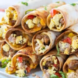 A stack of egg and sausage breakfast taquitos stacked on a white plate.