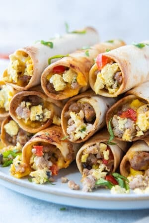 A stack of egg and sausage breakfast taquitos stacked on a white plate.