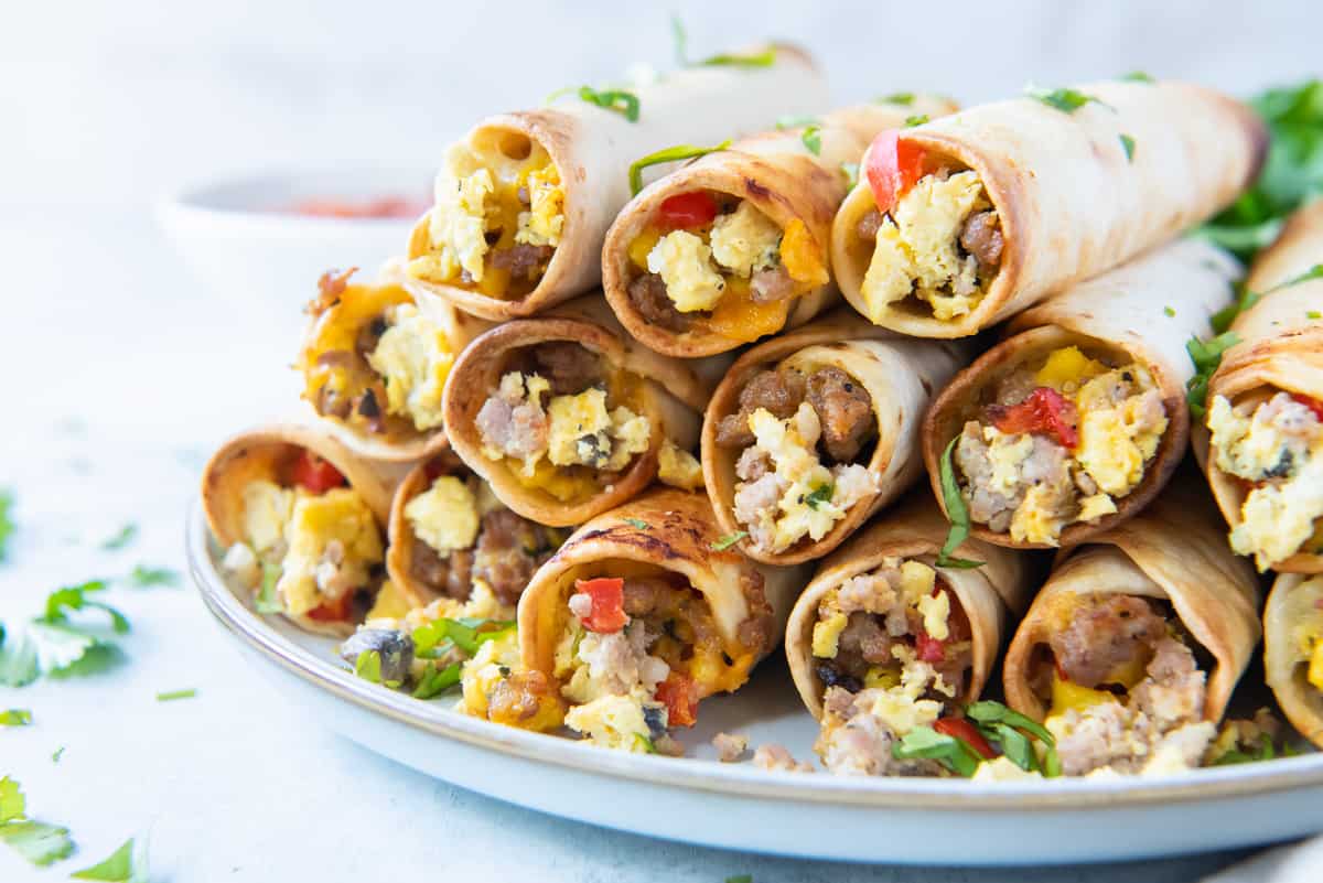 A stack of egg and sausage breakfast taquitos stacked on a white plate.