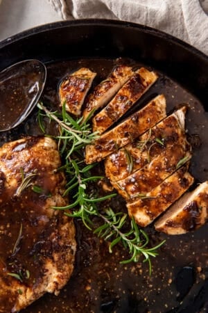A sliced chicken breast in balsamic glaze in a cast iron pan with sprigs of rosemary.