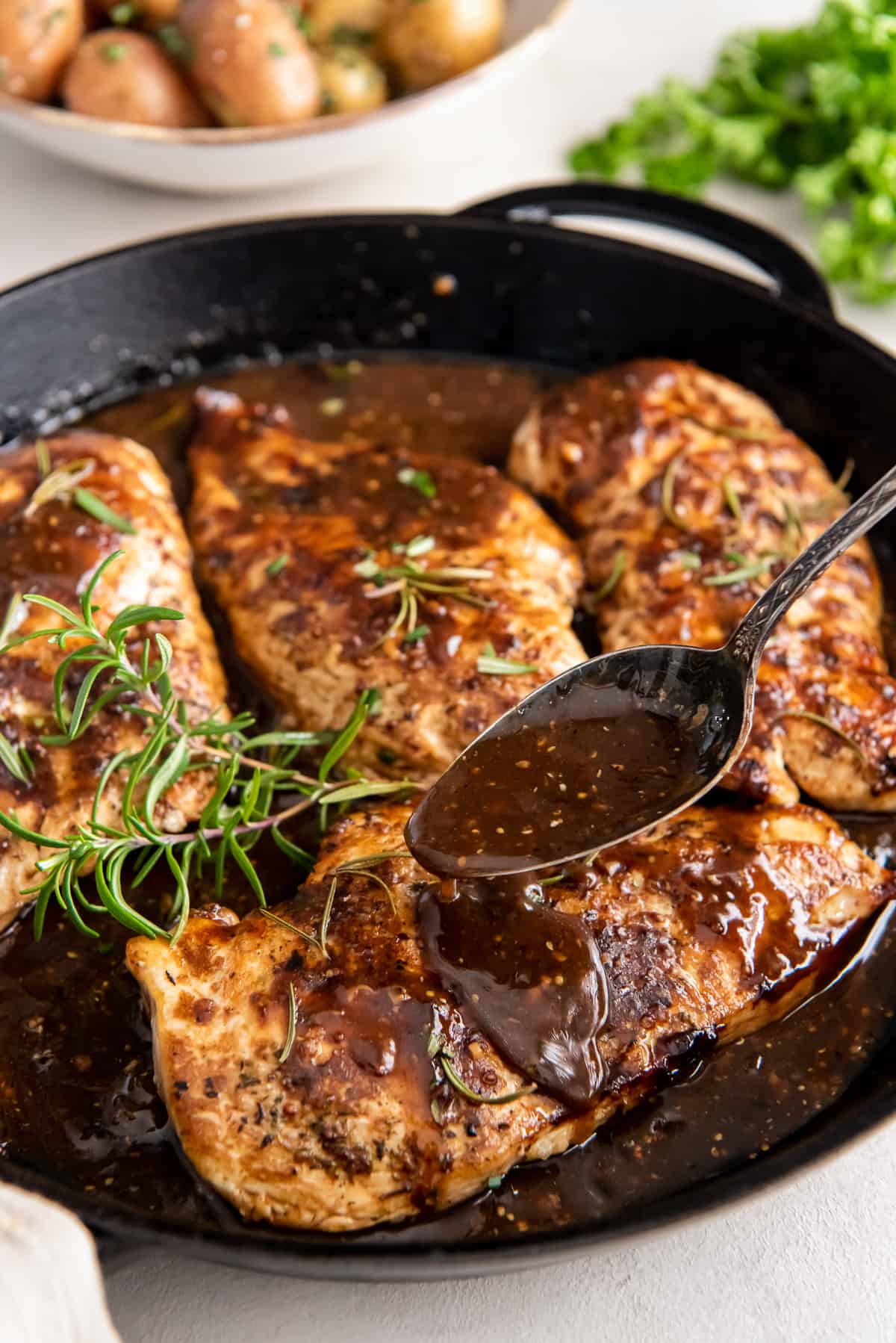 A spoon pouring balsamic glaze over chicken in a cast iron skillet.