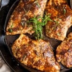 A closeup top down shot of chicken in balsamic sauce topped with sprigs of rosemary in a cast iron skillet.