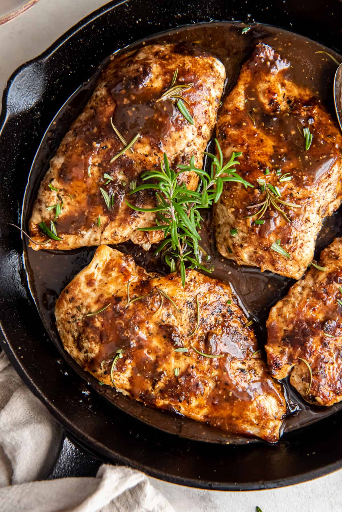 A close up of chicken in balsamic sauce topped with sprigs of rosemary in a cast iron skillet.