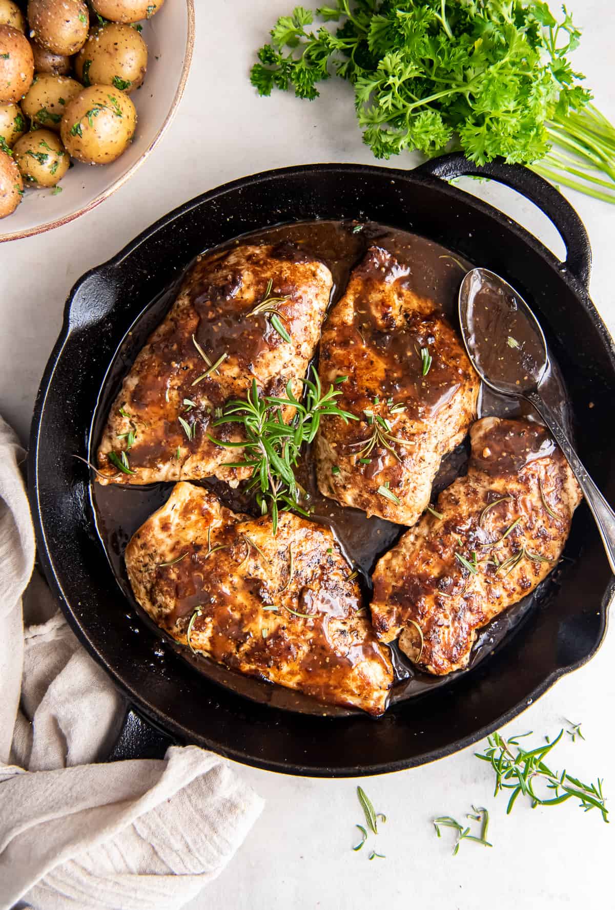 Chicken in balsamic sauce topped with sprigs of rosemary in a cast iron skillet.