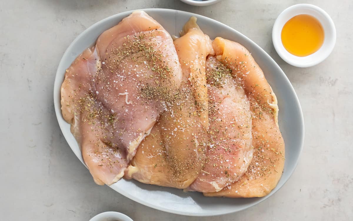 Seasoned pieces of boneless skinless chicken breast on a white plate.