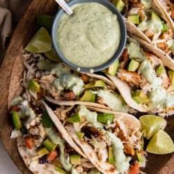 A top down shot of blackened fish tacos on a wood board with a small bowl of cilantro lime sauce.