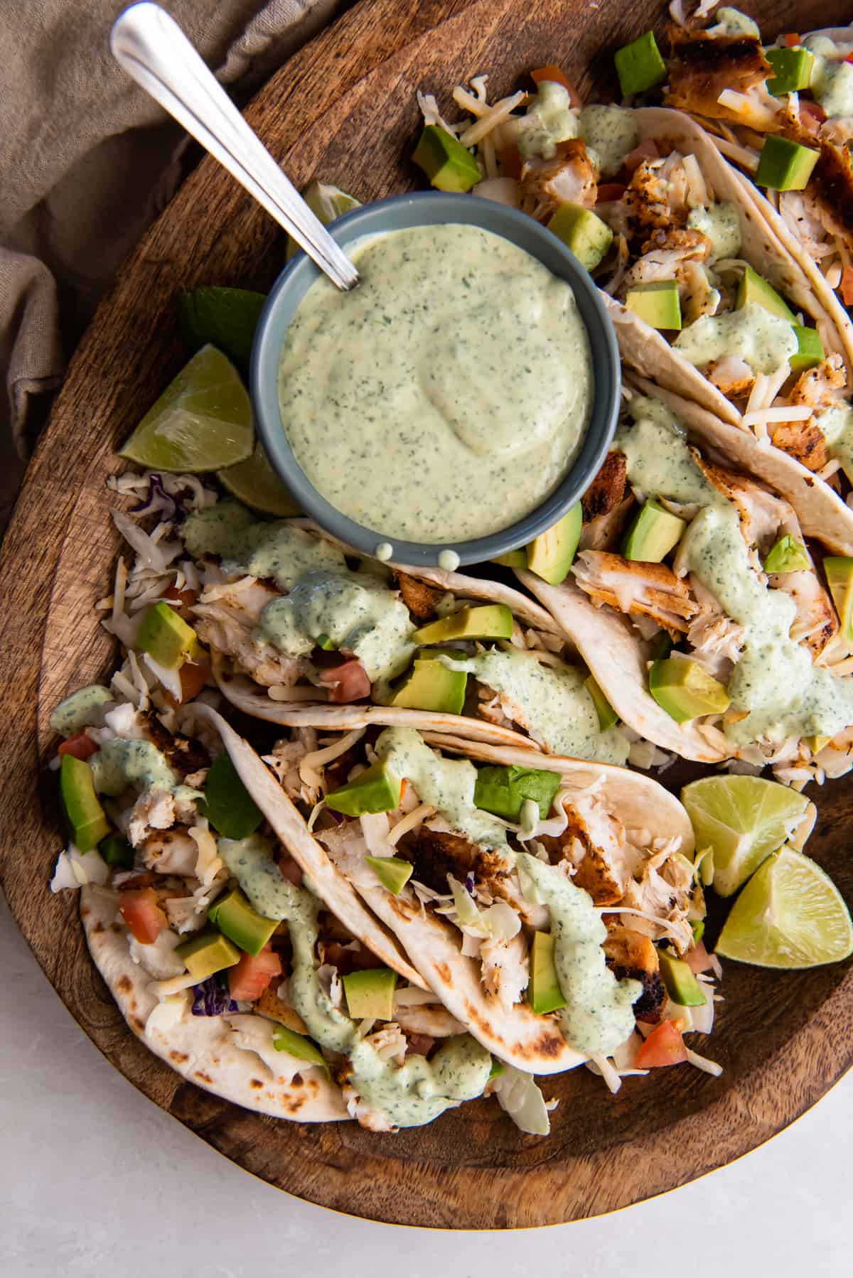 A top down shot of blackened fish tacos on a wood board with a small bowl of cilantro lime sauce.