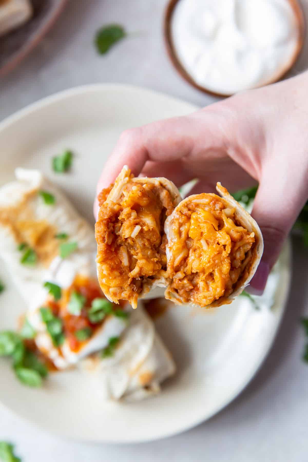 A top down shot of a hand holding two halves of a burrito so that you can see the filling of refried beans, rice, and cheese.