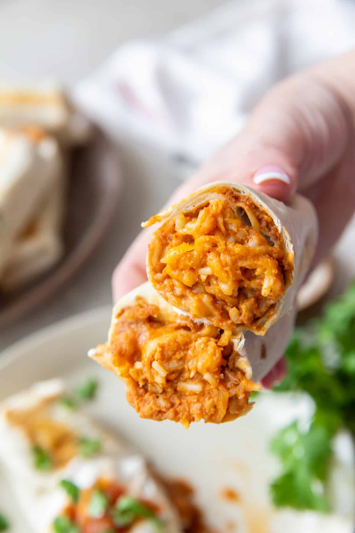 A hand holding two halves of a burrito so that you can see the filling of refried beans, rice, and cheese.