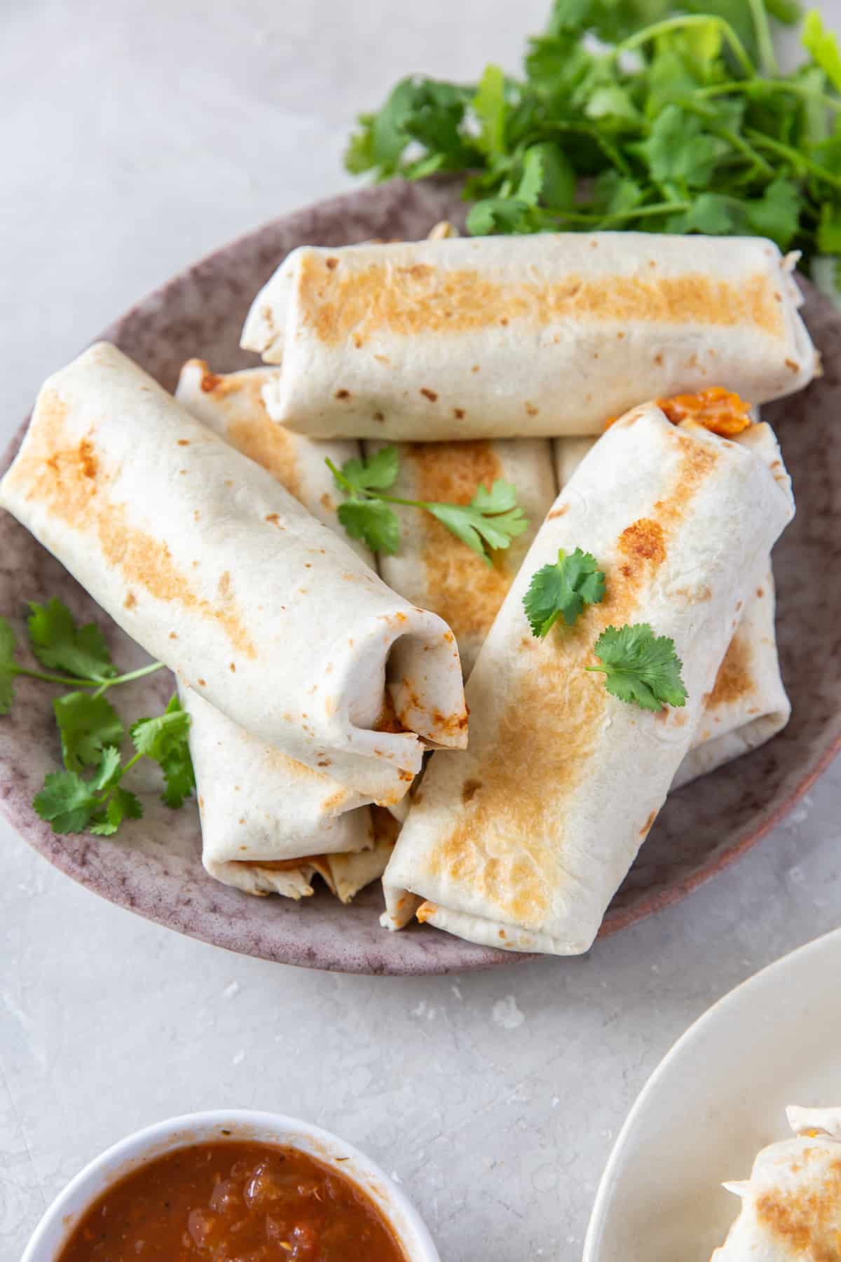 Baked burritos piled on a serving platter with cilantro.