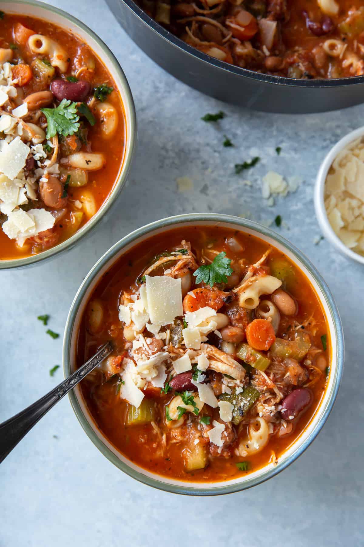 A top down shot of two bowls of chicken minestrone soup topped with shaved Parmesan cheese.