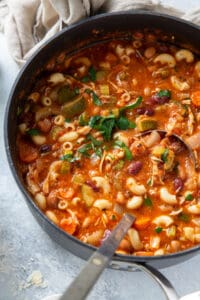 A top down shot of a large pot filled with minestrone soup with chicken and pasta.