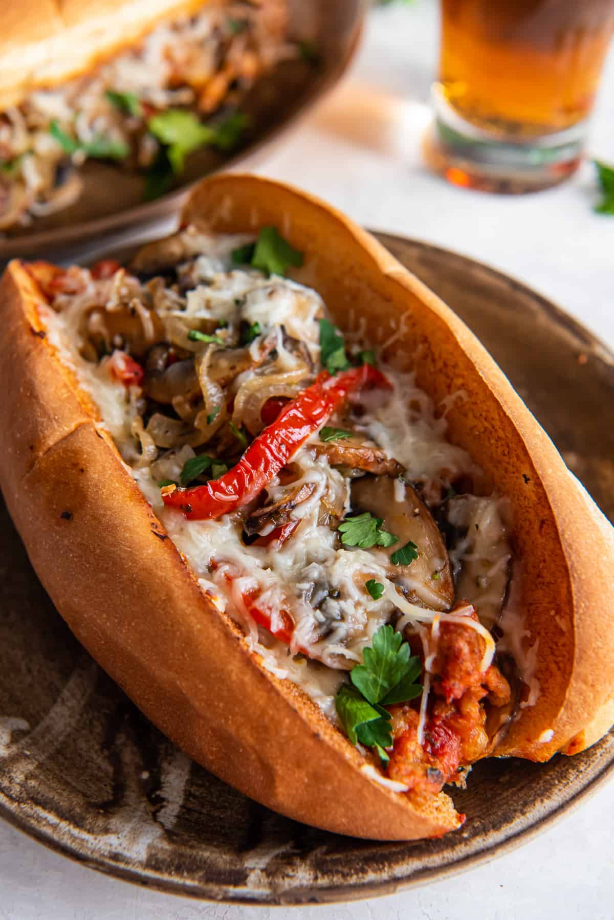 Ein italienisches Wurstsandwich mit Paprika, Zwiebeln, Pilzen und geschmolzenem Käse auf einer Platte.