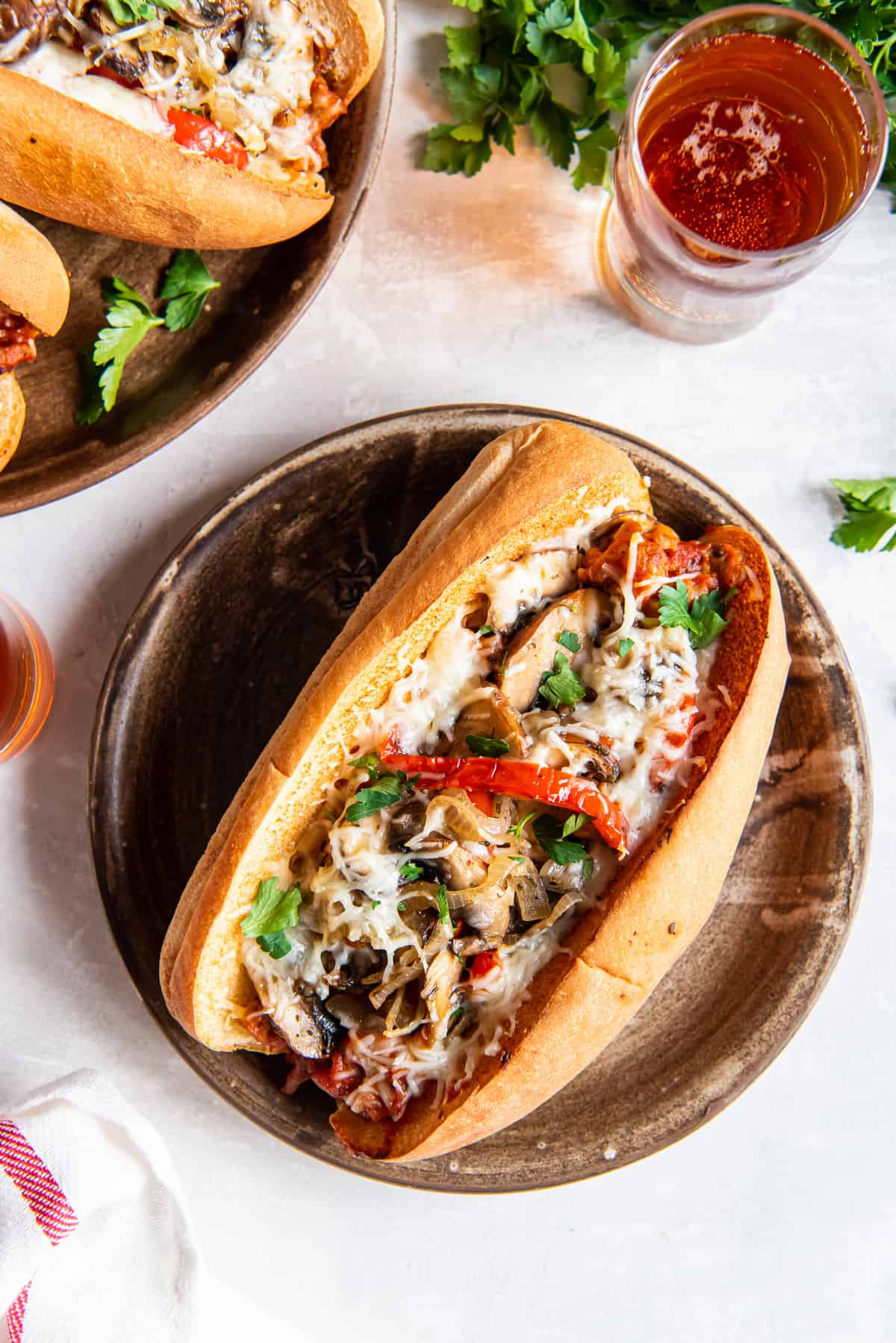 A top down shot of an Italian Sausage Sandwich on a plate next to a glass of beer.