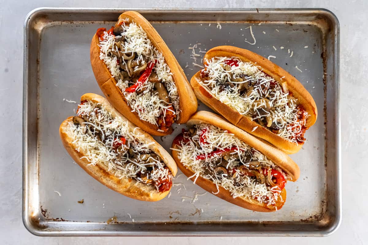 Ein Top-Down-Schuss von vier italienischen Wurstsandwiches mit geriebenem Käse auf einem Backblech.