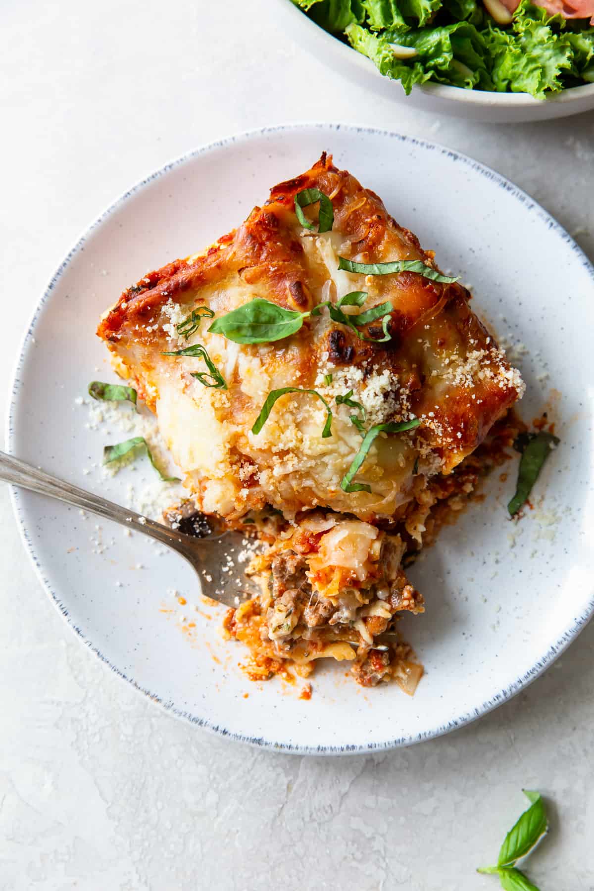 A top down shot of a piece of lasagna on a plate with a fork digging into it.