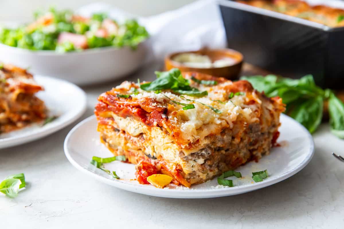 A piece of lasagna topped with fresh basil on a white plate.