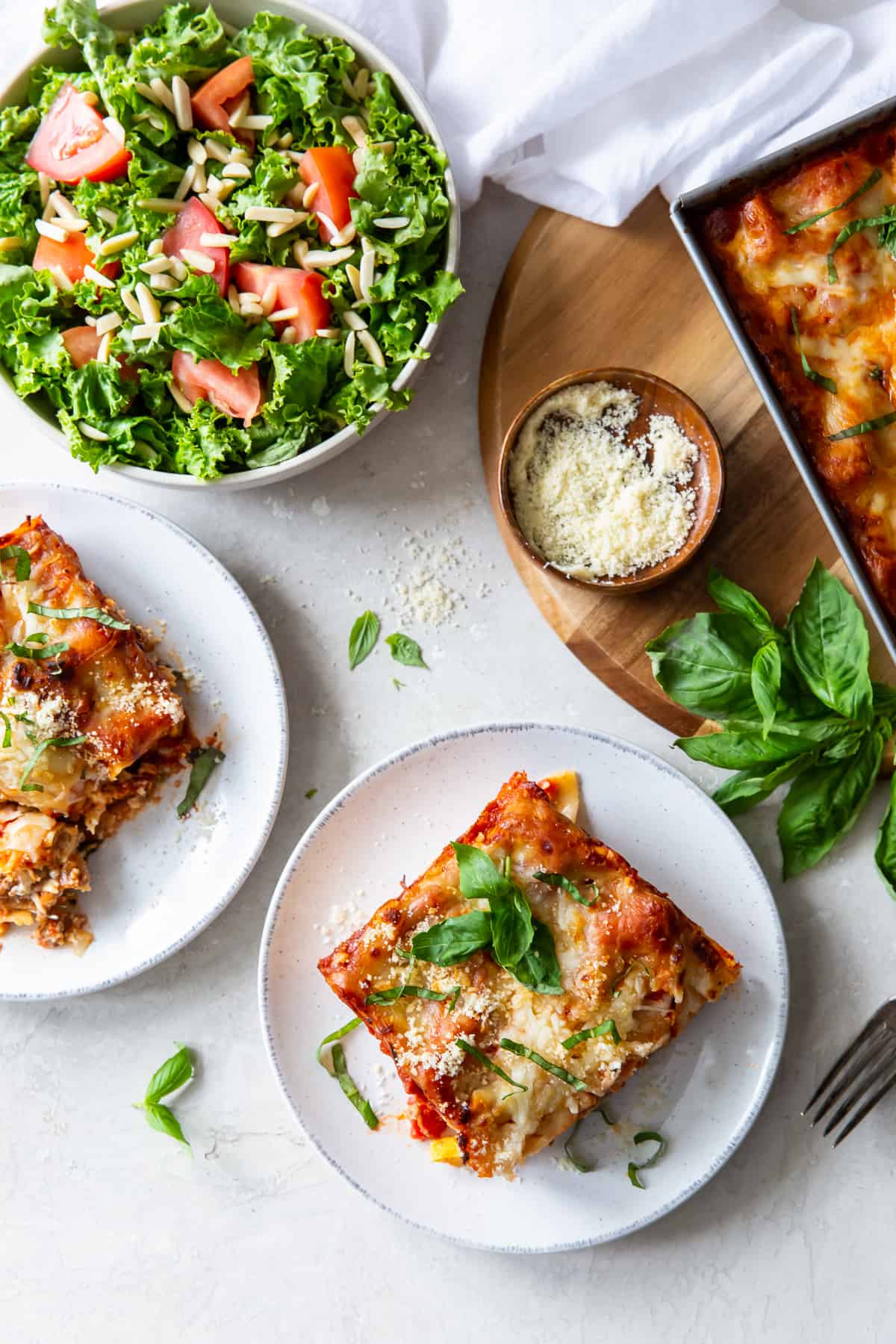 A top down shot of lasagna on two dinner plates next to a bowl of green salad.