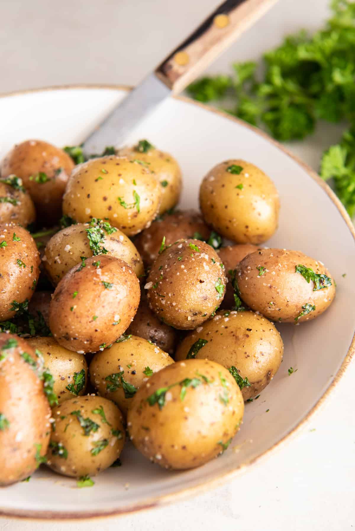 Parsley potatoes in a white bowl with a spoon.