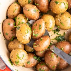 A top down shot of parsley potatoes in a Dutch oven with a spoon.