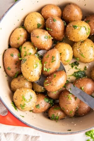 A top down shot of parsley potatoes in a Dutch oven with a spoon.