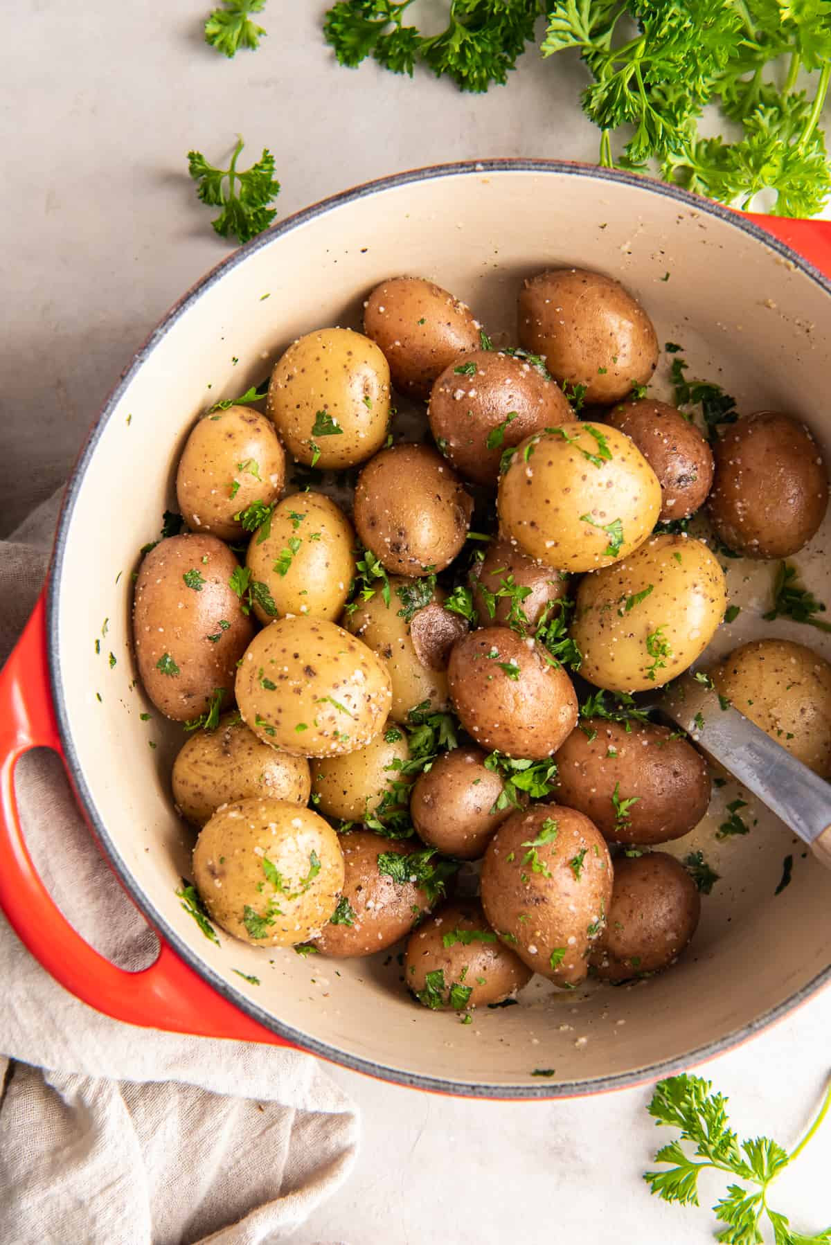 A top down shot of parsley potatoes in a Dutch oven with a spoon.