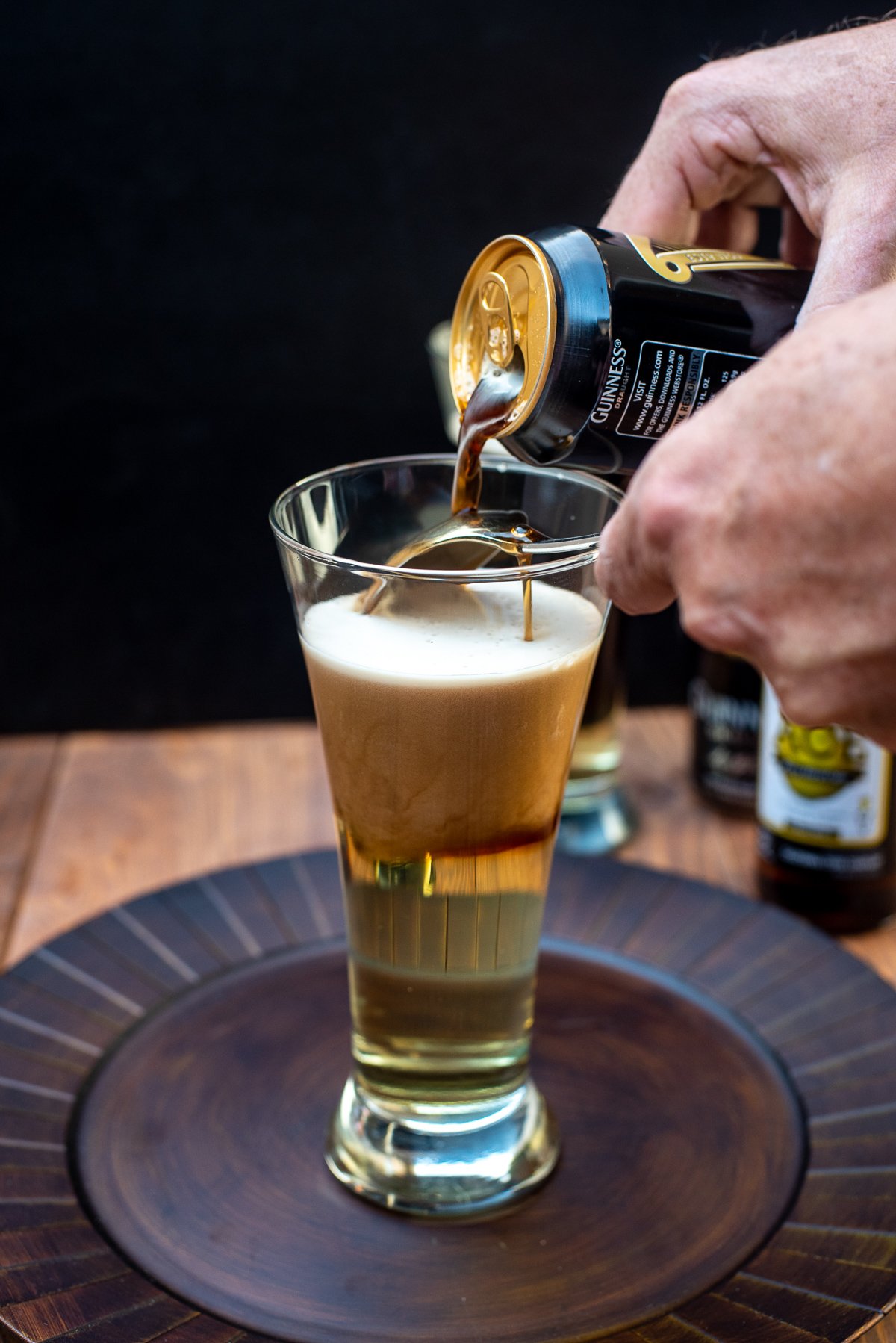 Guinness being poured from a can over a spoon and into a beer glass on top of a hard cider forming layers.