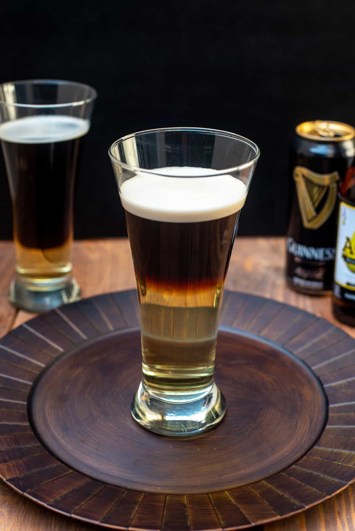 A Guinness and hard cider cocktail in a beer glass on a brown platter.