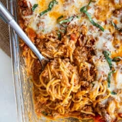 A top down shot of a spoon resting in a casserole dish full of spaghetti.